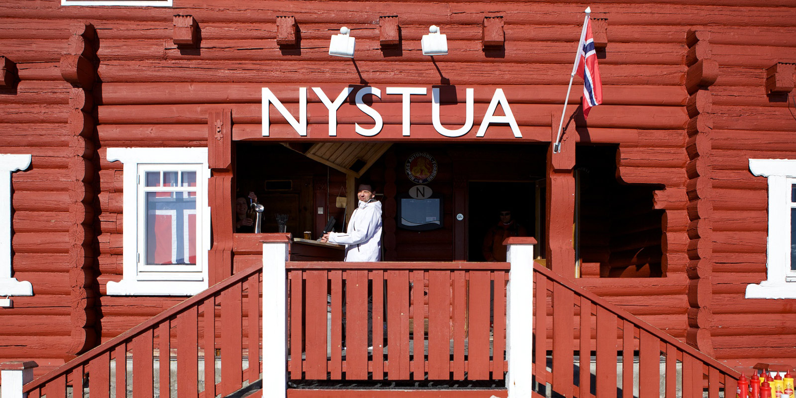 Nystua inngang rødmalt lokale med hvite vinduer og kokk