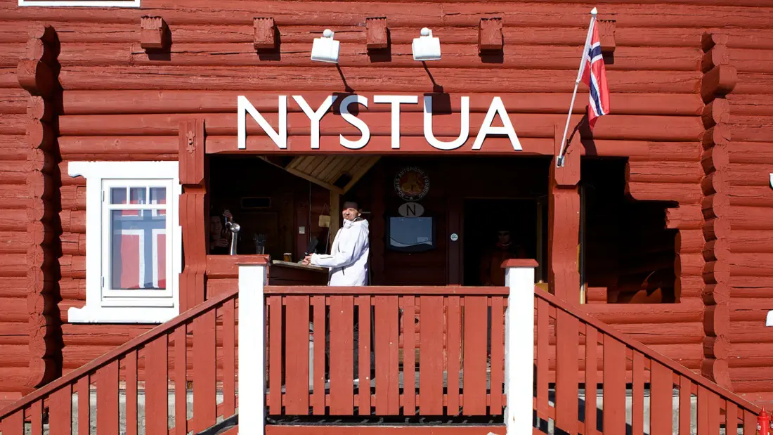 Nystua inngang rødmalt lokale med hvite vinduer og kokk
