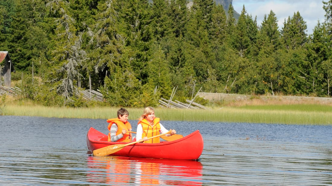 To mennesker som padler en rød kano i solskinn