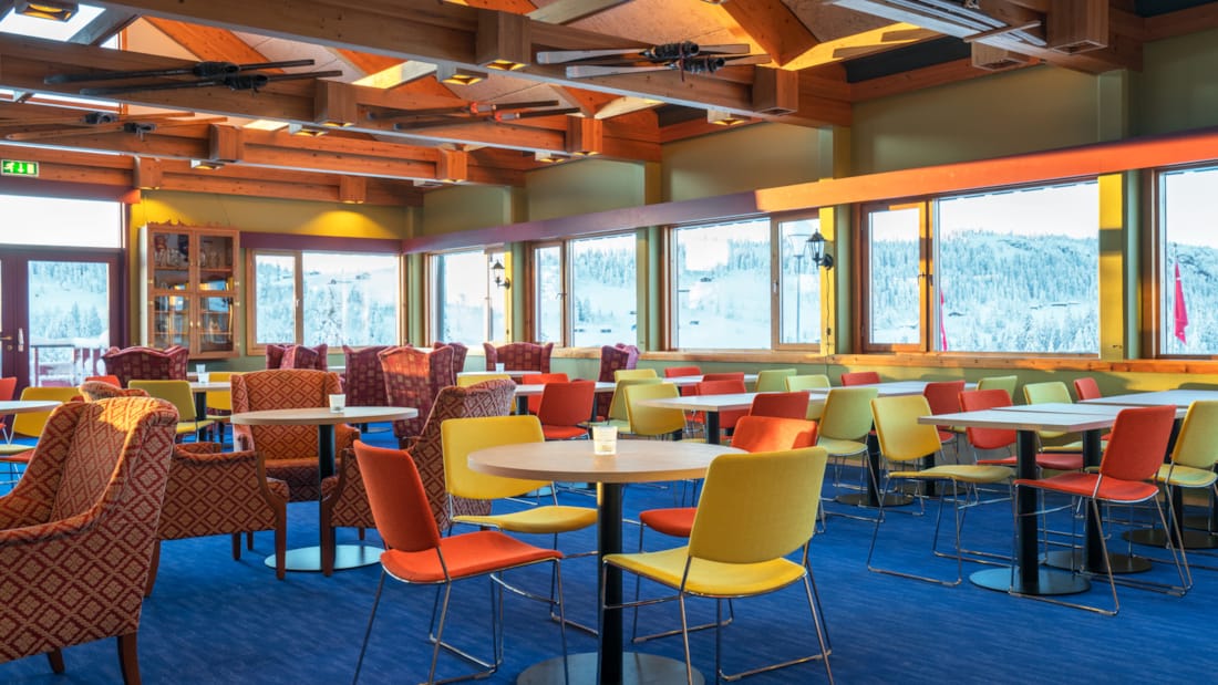 Spiseplass med fargerike stoler, stort maleri av skeikampen på veggen og store vinduer som ser ut mot landskapet på Austlid fjellstue