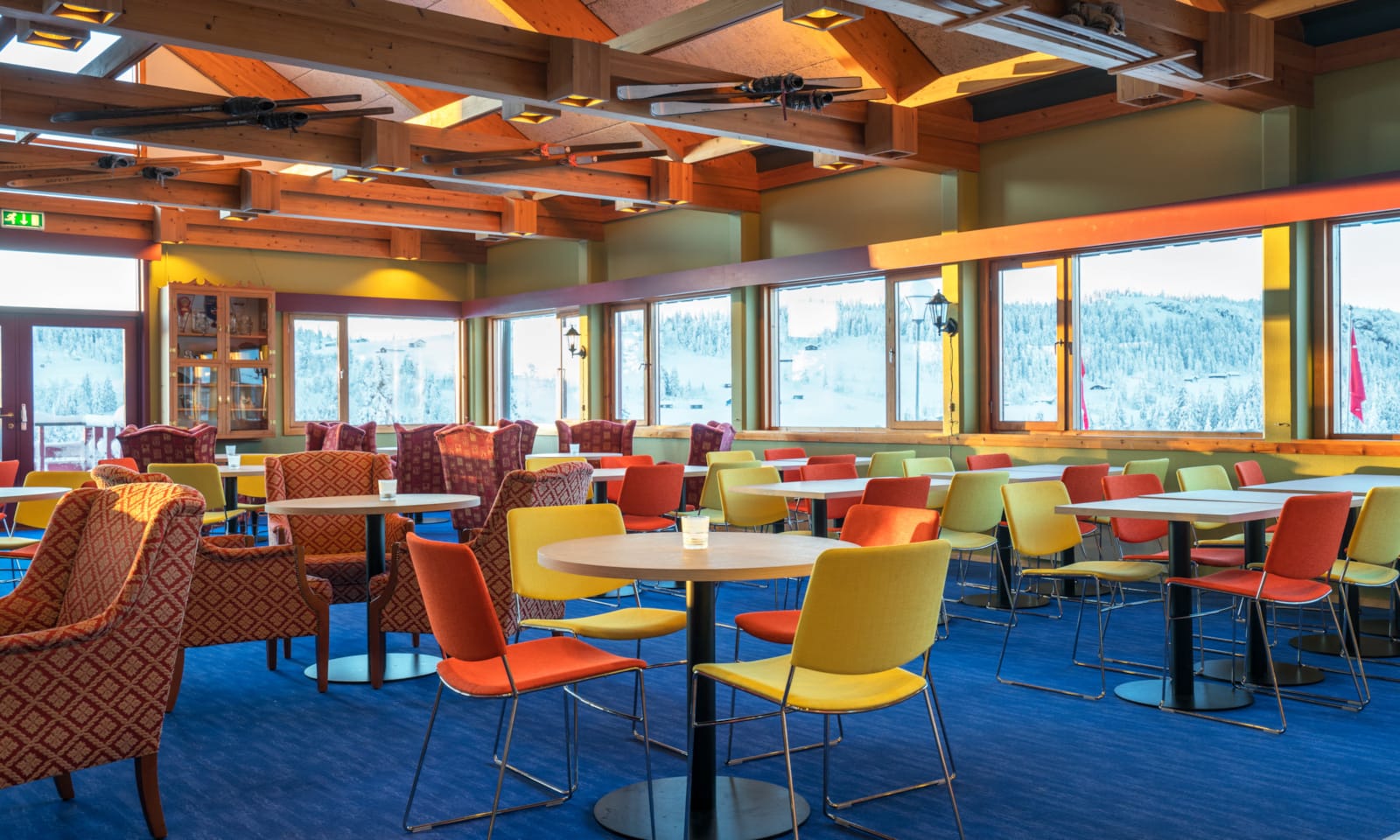 Spiseplass med fargerike stoler, stort maleri av skeikampen på veggen og store vinduer som ser ut mot landskapet på Austlid fjellstue