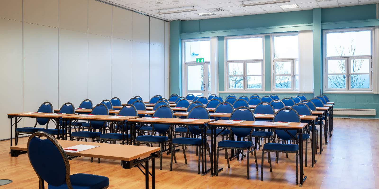 Rader med blå stoler og bord i lyst blått rom med vindusutsikt 