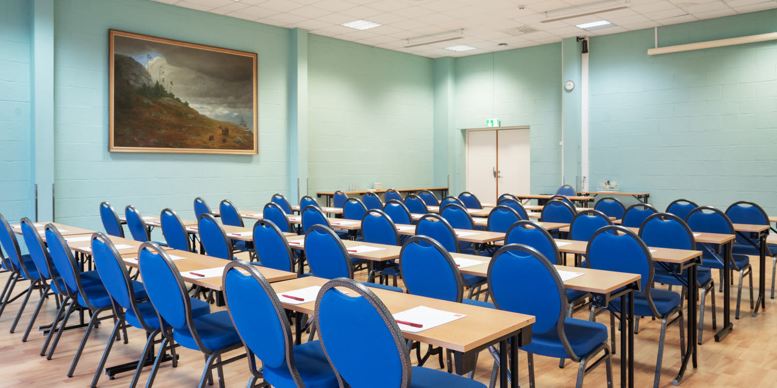 Rader med blå stoler og bord i lyst blått rom med et naturalistisk maleri på veggen