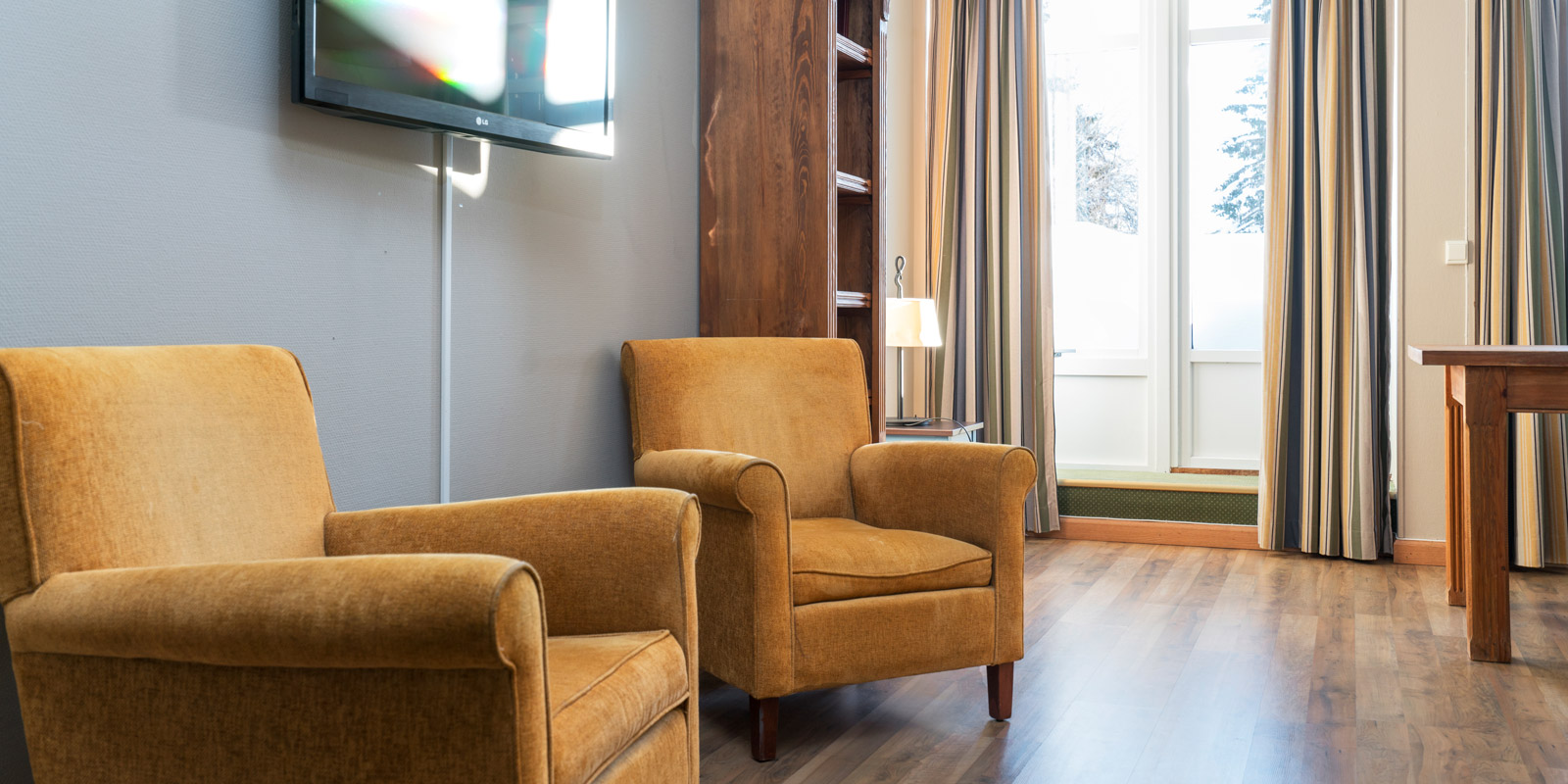 TV, to lenestoler og verandad&#xF8;r med store vinduer i buisnessrom p&#xE5; Thon Hotel Skeikampen