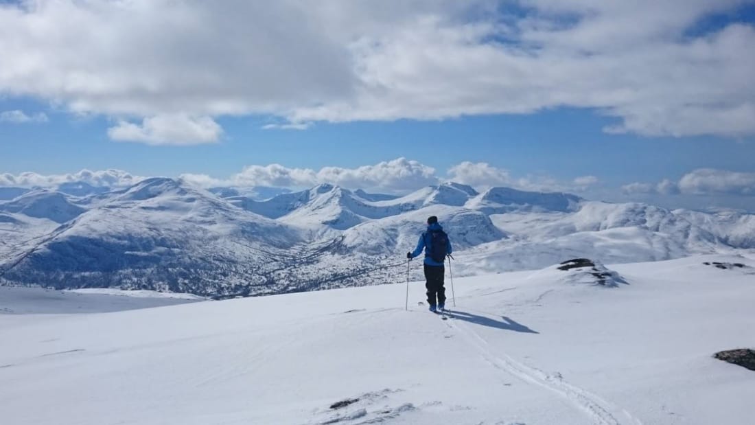 Snø, sol og person i vinterlandskap med fjell i bakgrunnen