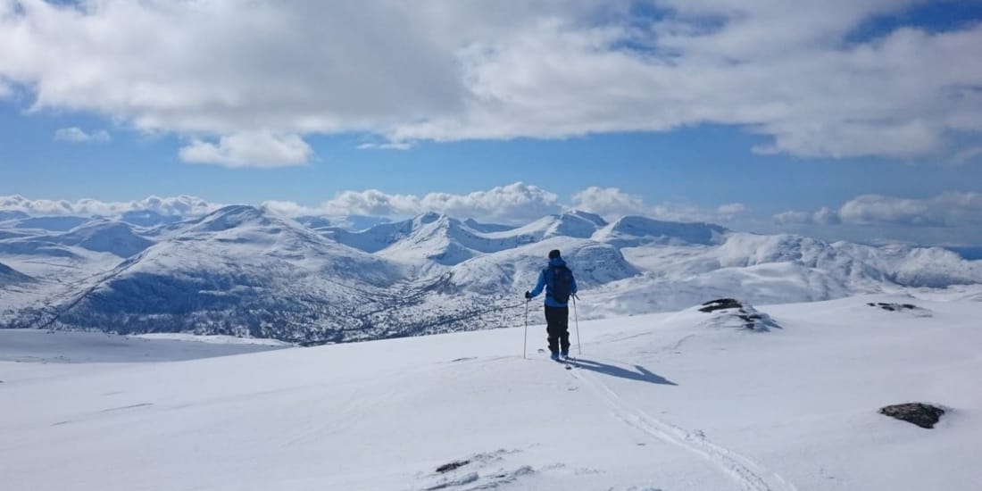 Snø, sol og person i vinterlandskap med fjell i bakgrunnen