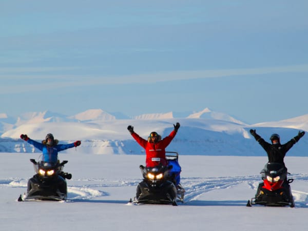 En gruppe mennesker kjører snøscootere på en snødekt sti.