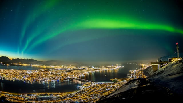 Nordlys som skinner over Tromsø by på kveldstid, sett fra avstand
