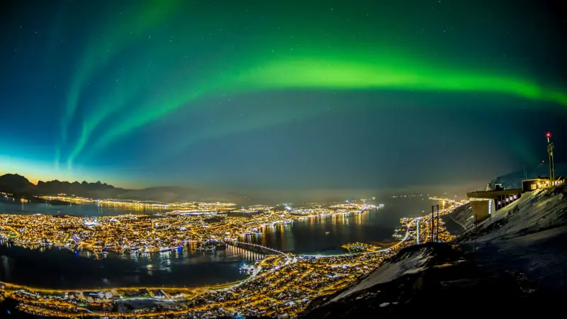 Nordlys som skinner over Tromsø by på kveldstid, sett fra avstand