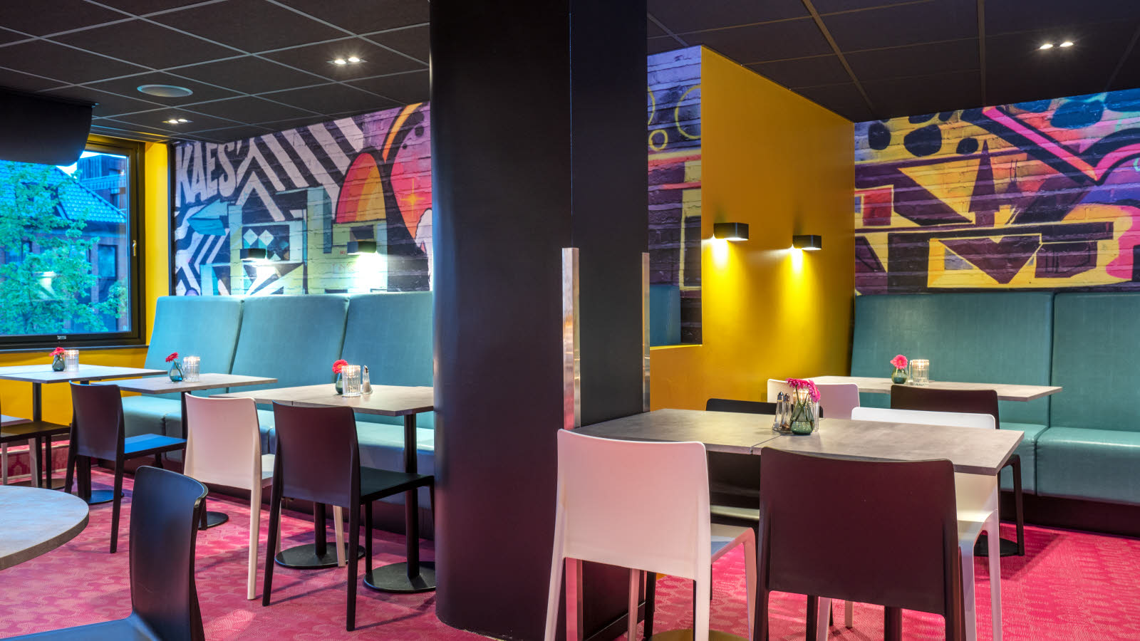 Frokostsalen hos Thon Hotel Trondheim. Veggene er malt med grafittiuttrykk, turkise sofaer, hvite og sorte stoler, spisebord, rosa gulvteppe.