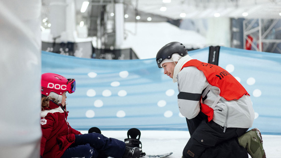 Barn med skiutstyr og voksen mann med vest i skianlegg