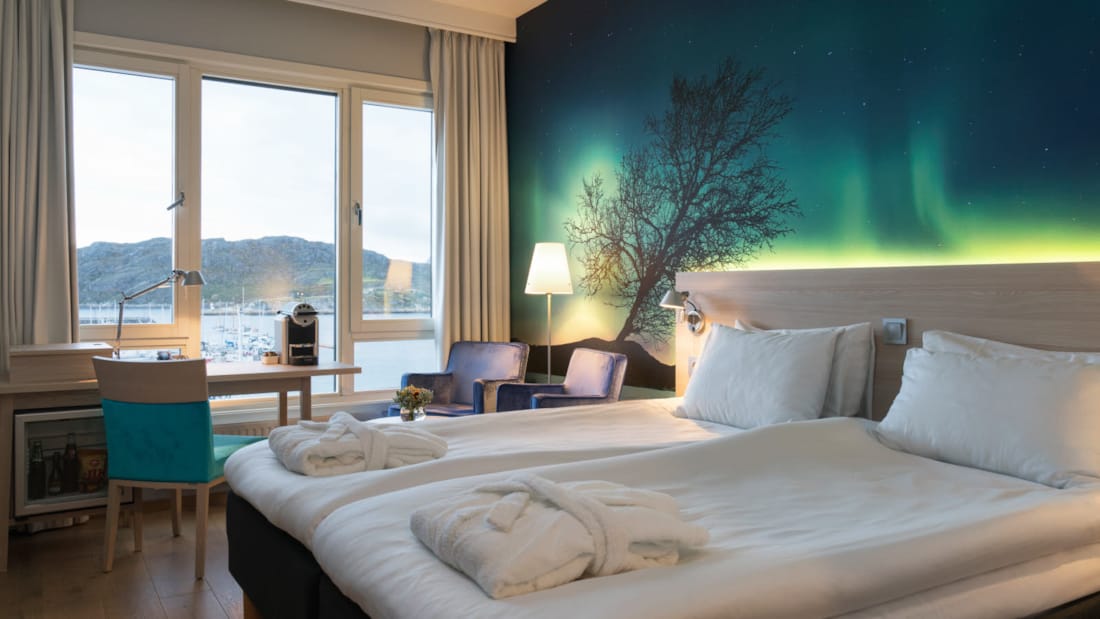 Superiorrom hos Thon Hotel Nordlys. Dobbeltseng med bilde av nordlys bak sengegavl, skrivebord og utsikt over sjøen.