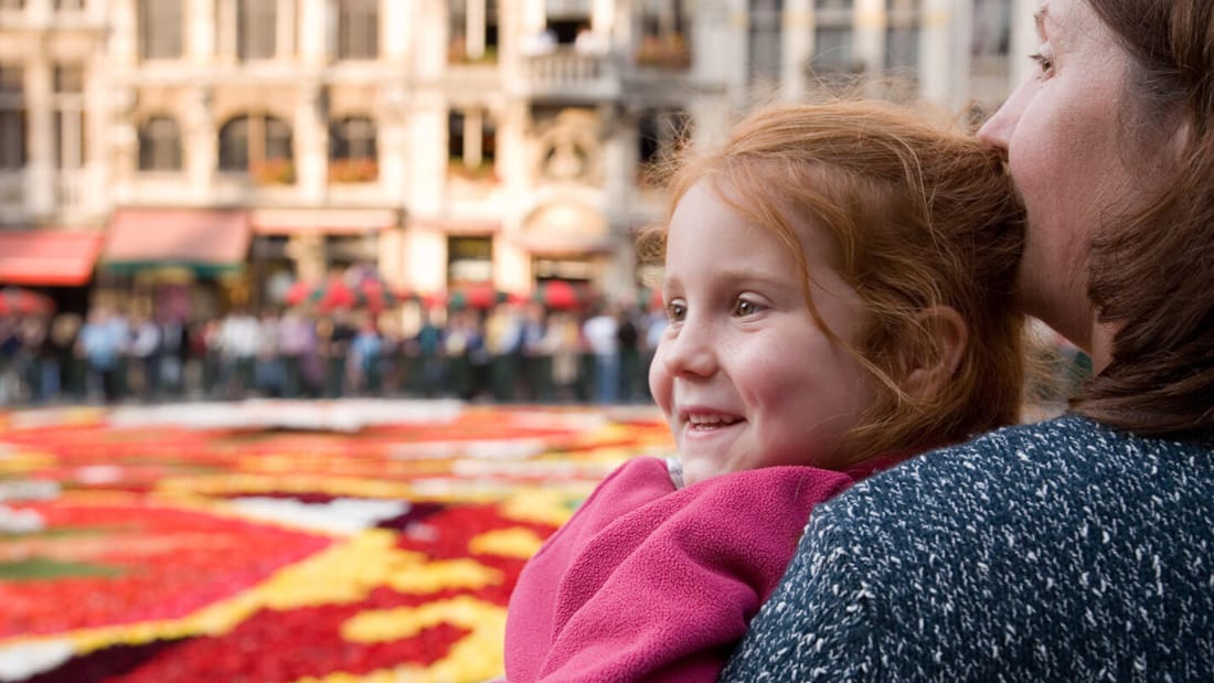 Liten jente med moren ser begeistret utover et fargerikt blomsterbed i Brussel
