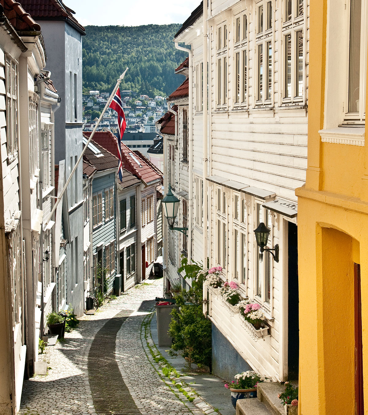 Et smug i gamlebyen i Bergen med norsk flagg og sol som skinner.