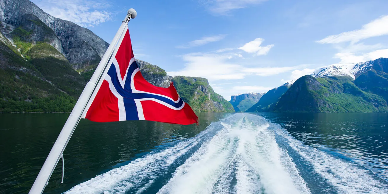 Fjord fra baksiden av en b&aring;t med et norsk flagg 