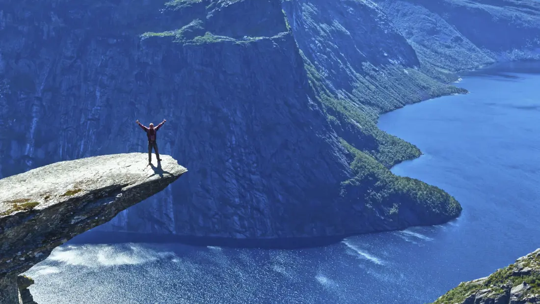 Menneske på Trolltunga foran fjord under blå himmel