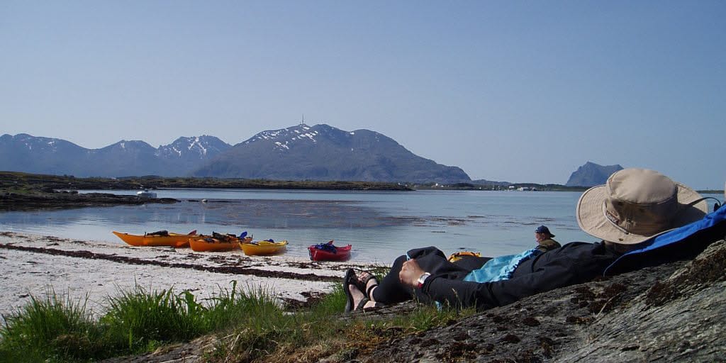 En person ligger på stranden med en kajakk i Brønnøysund