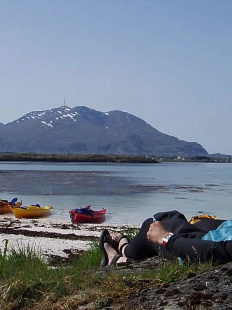 En person ligger på stranden med en kajakk i Brønnøysund
