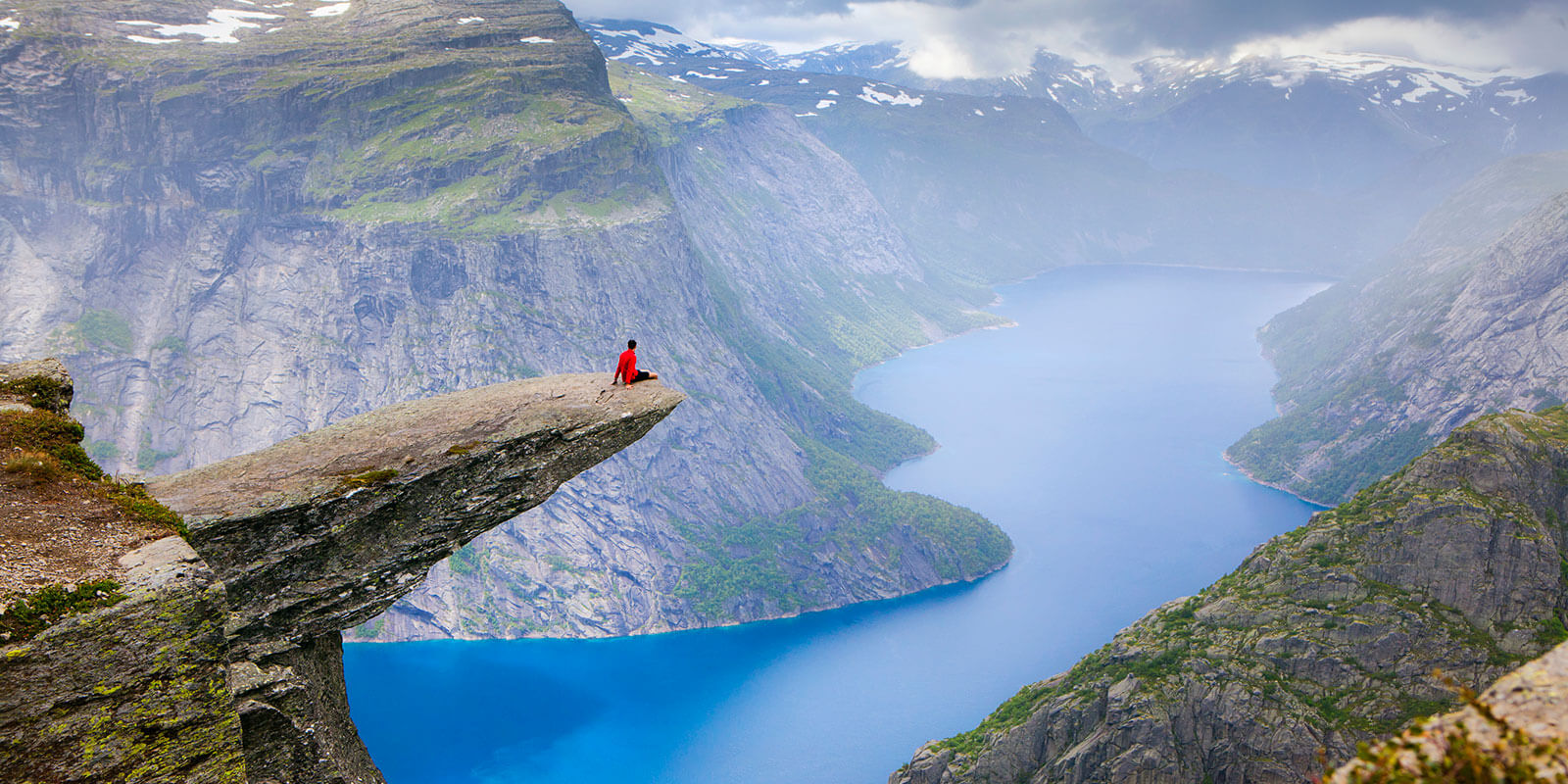 Et menneske sitter ytterst på Trolltunga og nyter utsikten