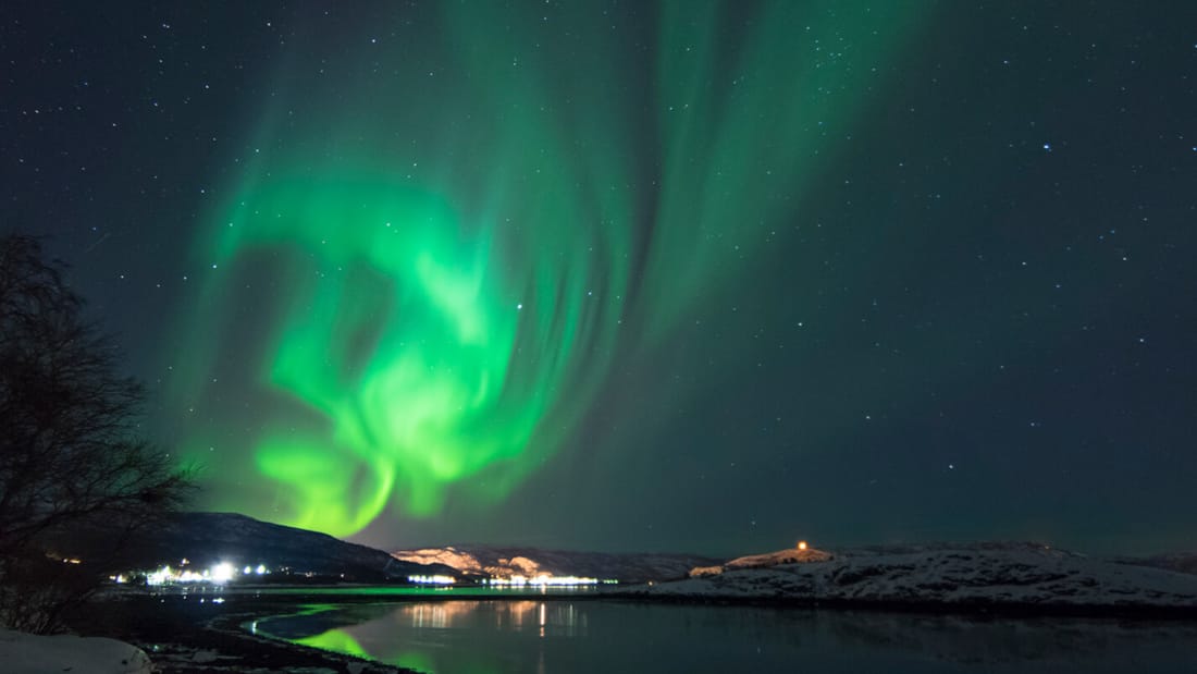 Nordlys som lyser over vann og fjell i vintermørket i Hammerfest