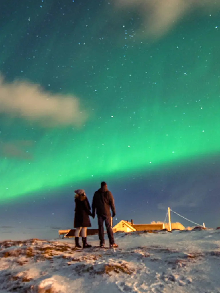 To personer som ser på nordlyset i Kirkenes på vinterstid, sett bakfra.