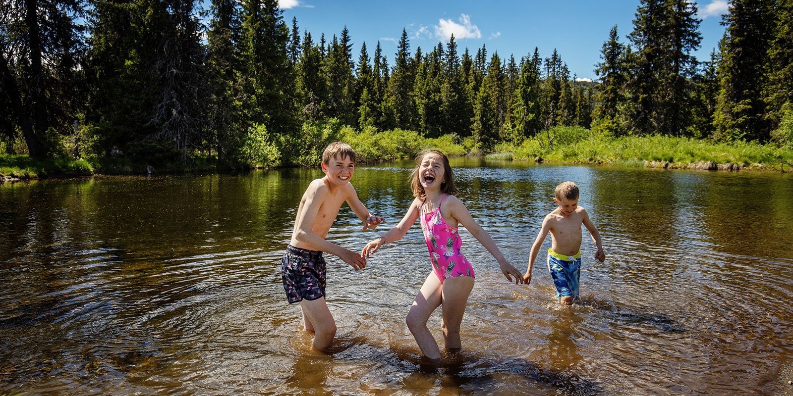 Tre barn som bader i et vann på Skeikampen