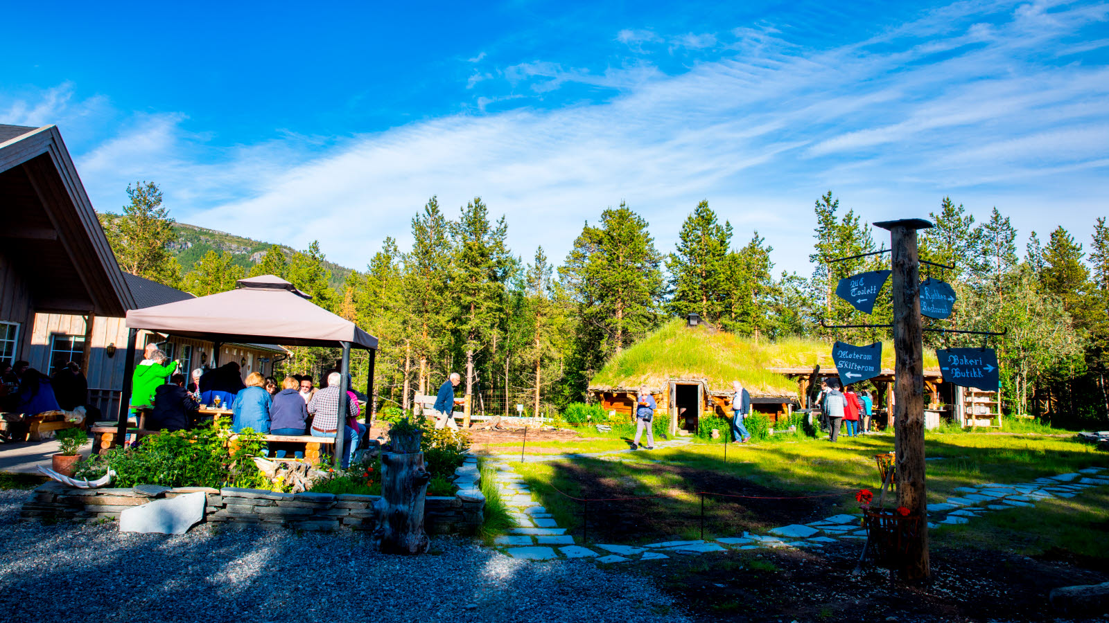 Gjester sitter og spiser på trebenker hos Trasti og Trine.