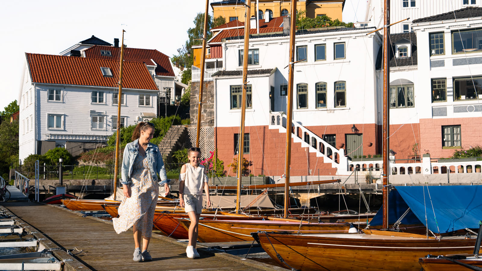 En kvinne og en jente går langs en brygge med båter.