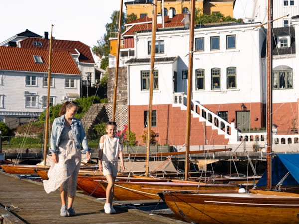 En kvinne og en jente går langs en brygge med båter.