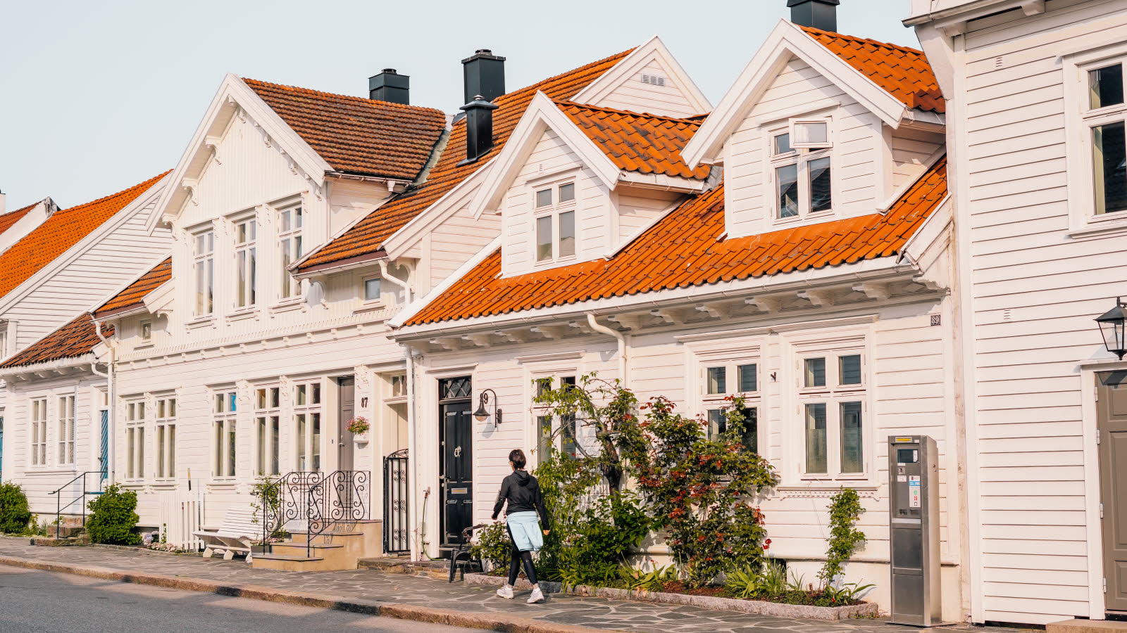 Posebyen i Kristiansand, med hvite, gamle trehus. En kvinne går på fortauet foran husene.