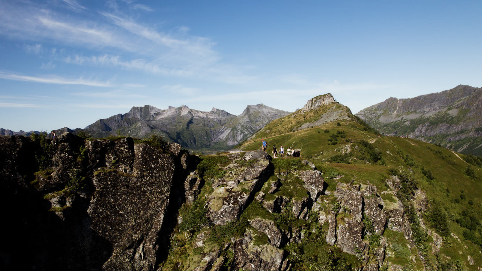 Turfølge på 7 personer på fjelltur i solskinnsvær i Lofoten. I bakgrunnen sees fjell.