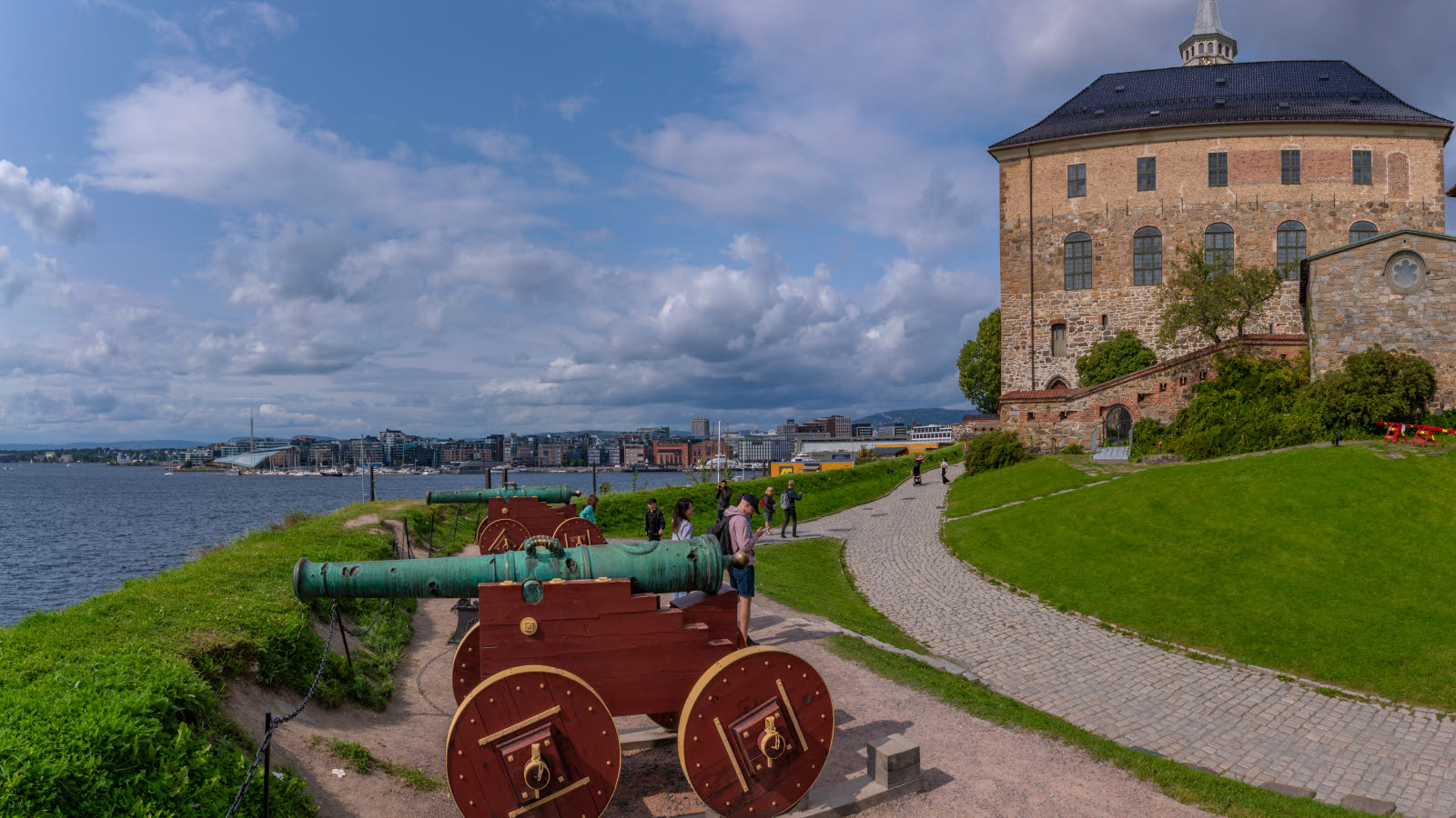 Utsikt over Akershus Festning en sommerdag. Kanoner i front og Tjuvholmen i bakgrunnen.