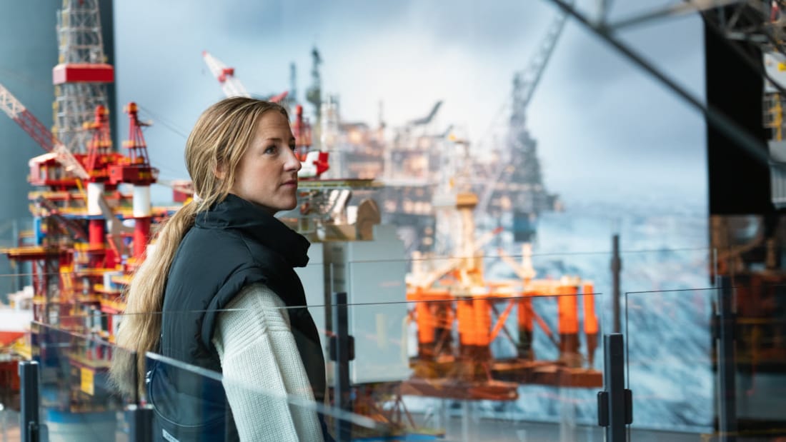 Kvinne står foran bilde og modell av oljeplattform inne på Oljemuseet i Stavanger.