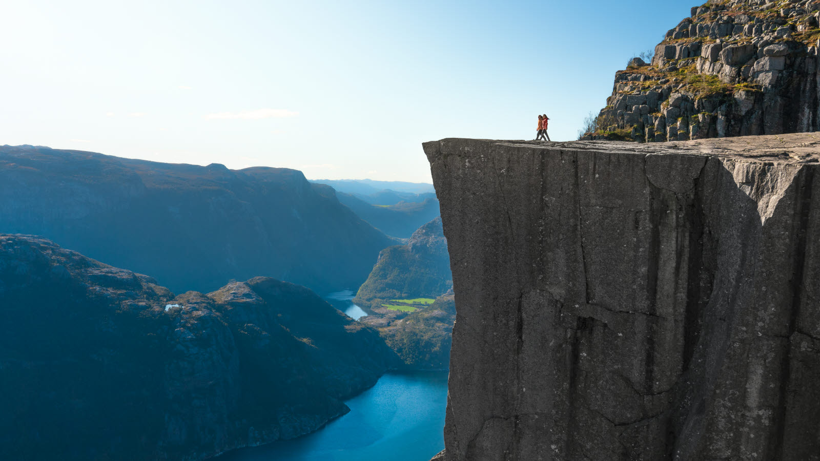 En mann står på kanten av en klippe (Preikestolen) og ser utover en innsjø.