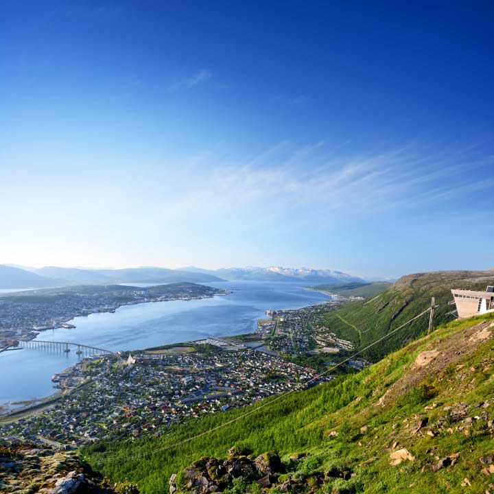 Utsikt over Tromsø by fra toppen av en ås. Byen ligger vakkert omgitt av fjell og hav.