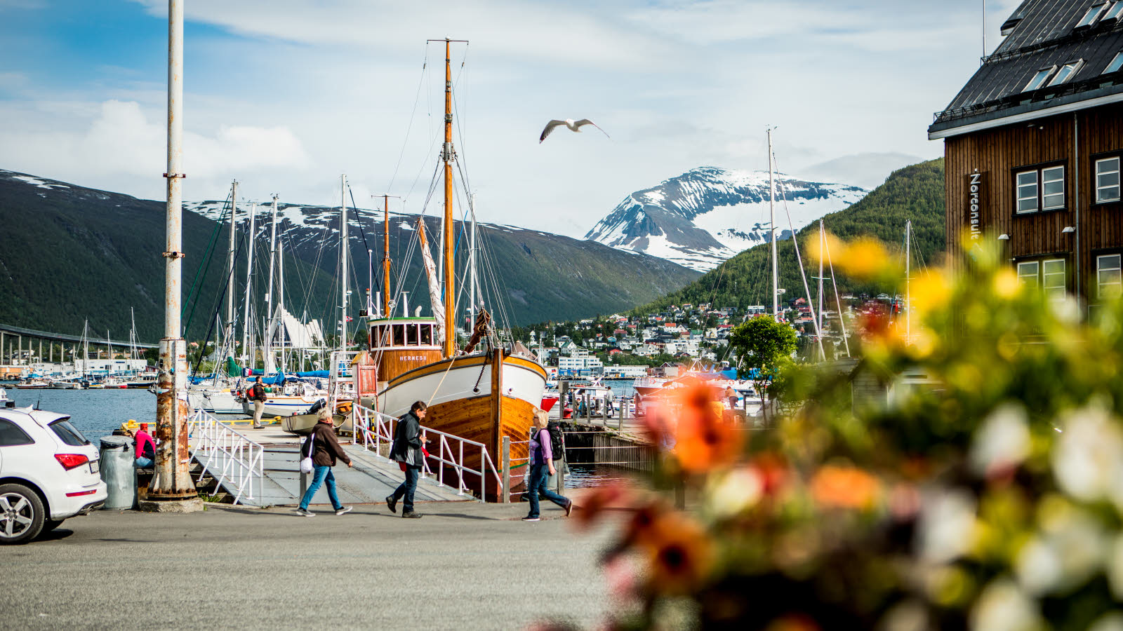 En fiskebåt ligger fortøyd ved en av bryggene i Tromsø. I bakgrunnen ses Ishavskatedralen, grønne fjell og noen fjell med snø.