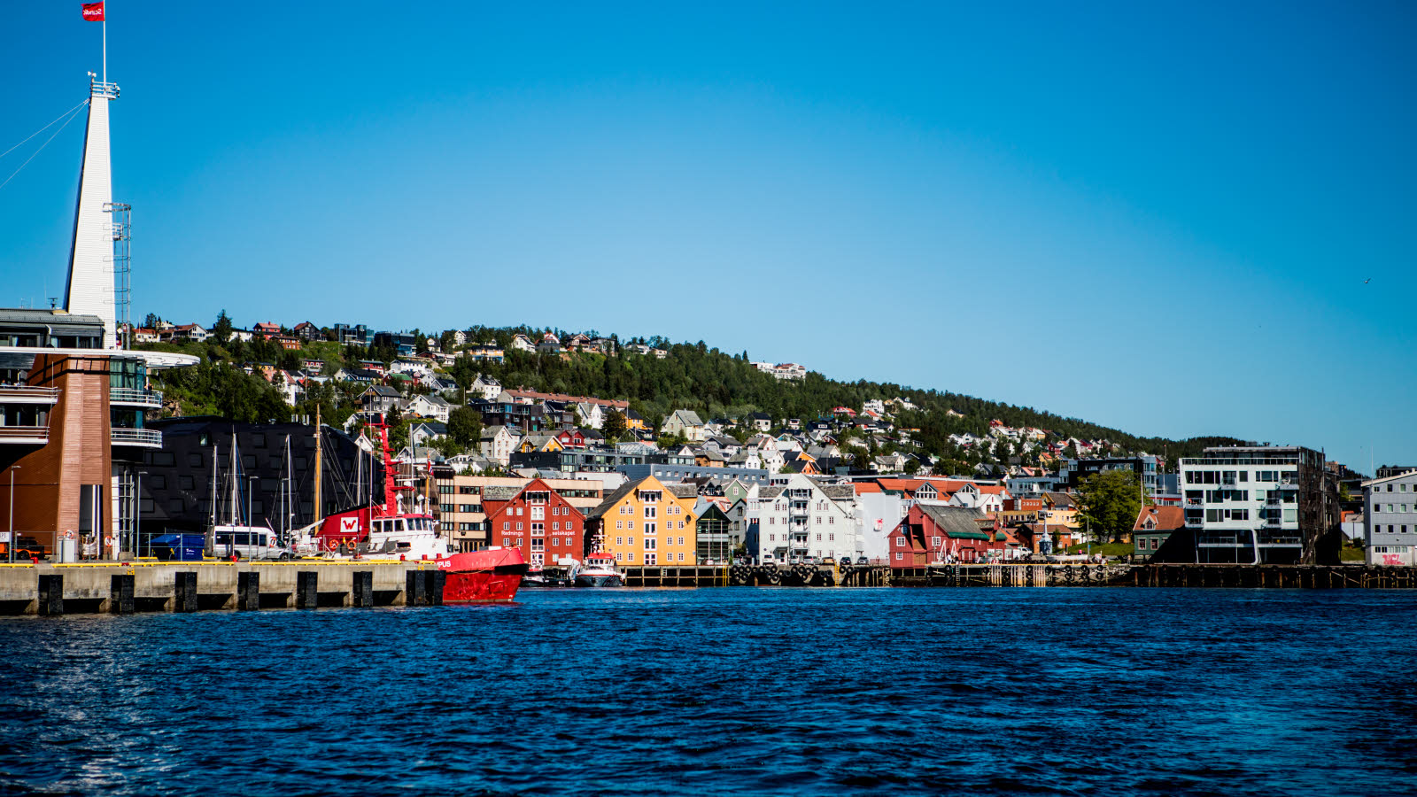 Eldre trebygg i sterke farger, som huser bl.a. Polarmuseet, langs vannet i Tromsø.