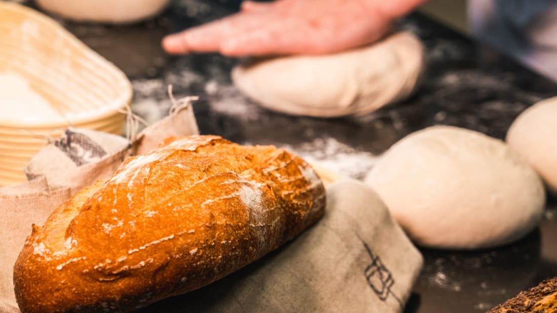 Nærbilde av hjemmelaget brød med hender som baker ut brød i bakgrunnen
