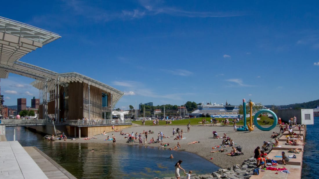 Mennesker koser seg ved vannet og på stranden på Tjuvholmen i Oslo.
