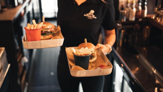 Servitør som holder en brett med burger og fries på