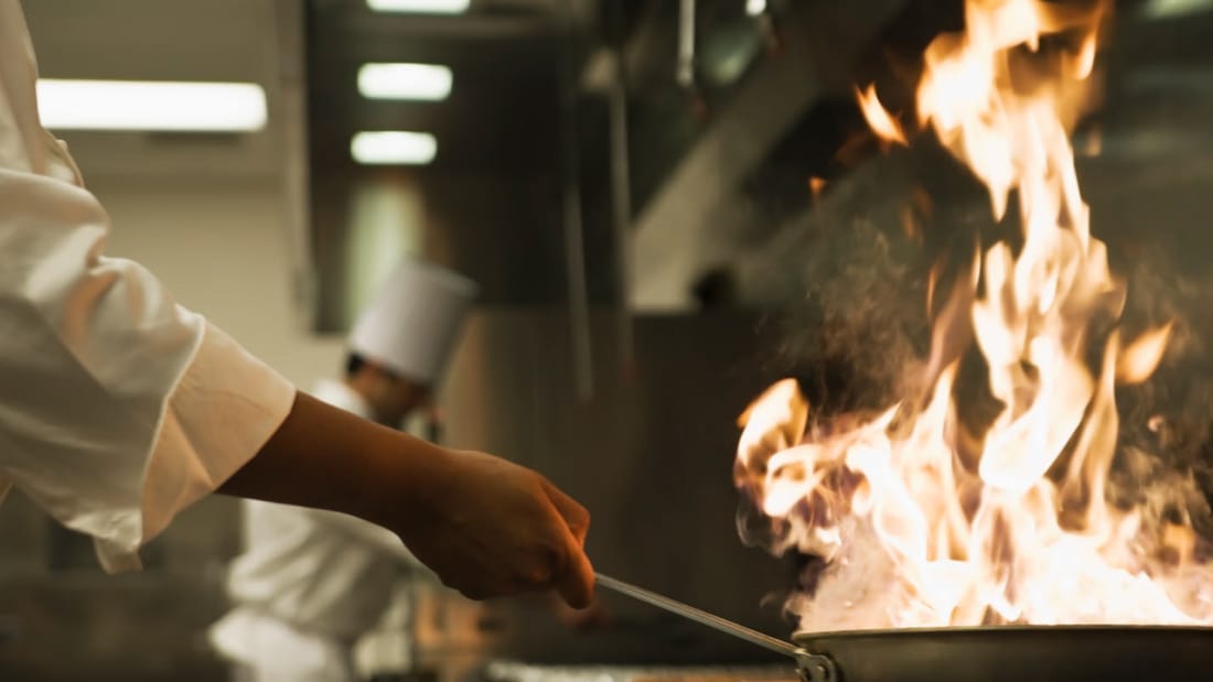 Kokk steker med flammer i stekepanne på restaurant