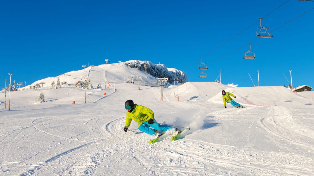 Skeikampen alpinesenter m ed to stk som står på ski nedover en bakke