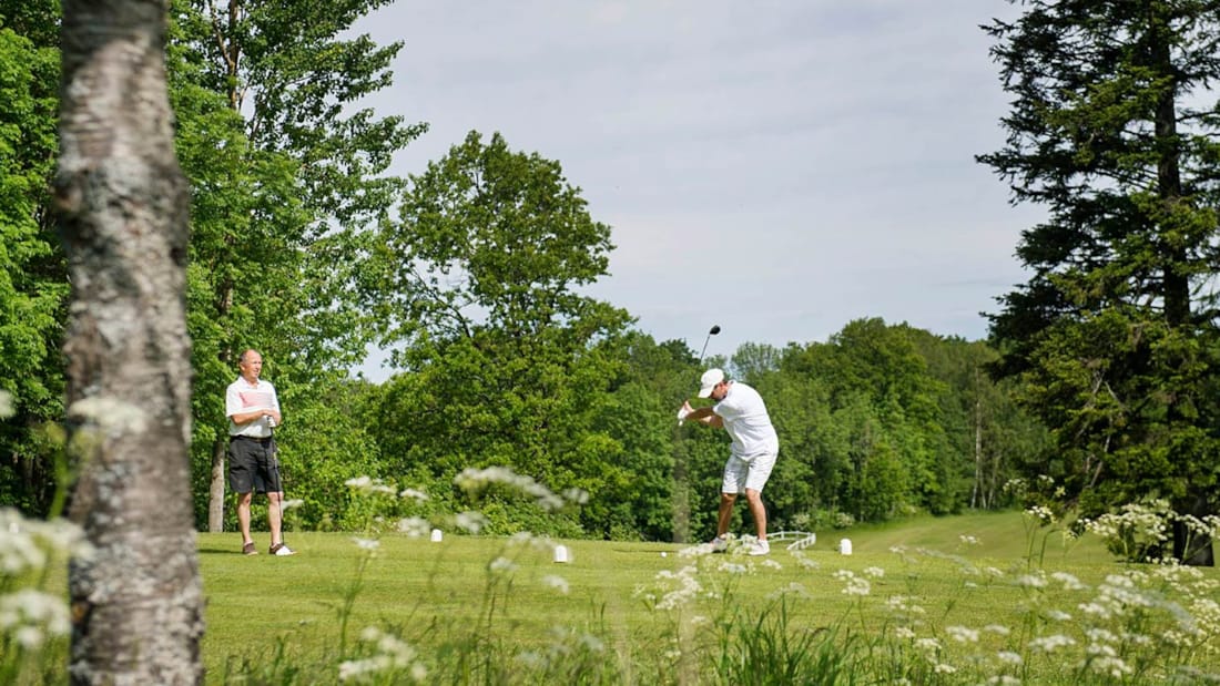 To menn som spiller golf i grønne omgivelser