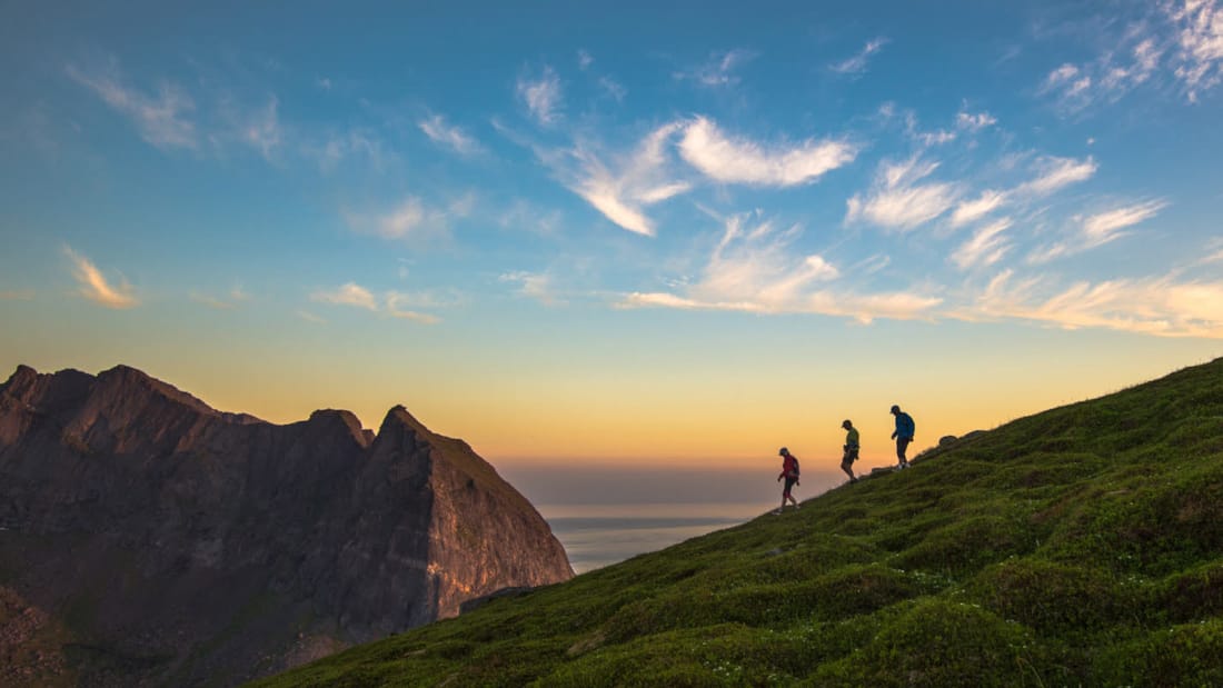 Tre mennesker som går ned en fjellside i solnedgang
