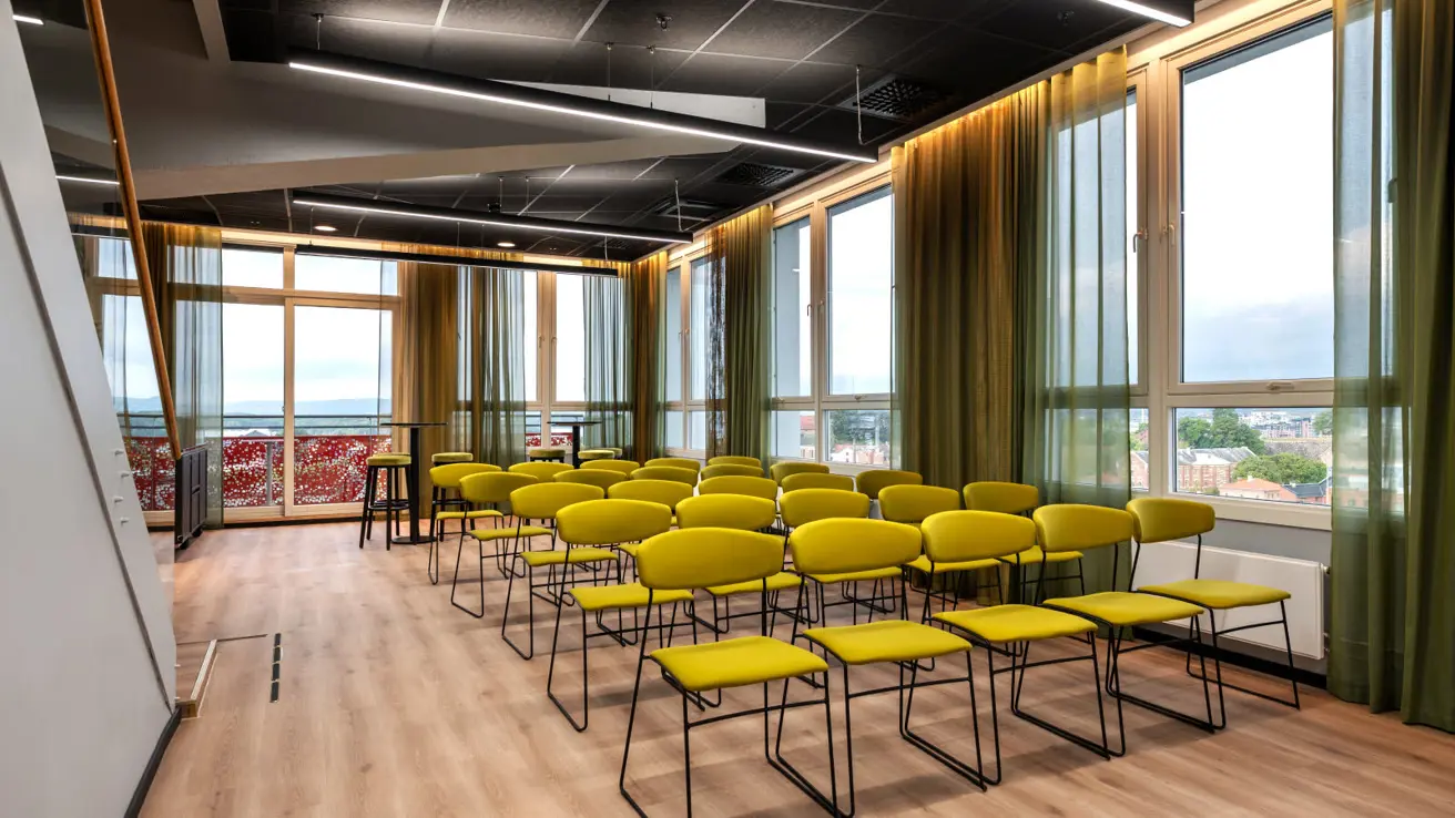 Møterom med gulgrønne stoler på rekke og rad og en flott utsikt fra vinduer som går hele veien bort på begge vegger.