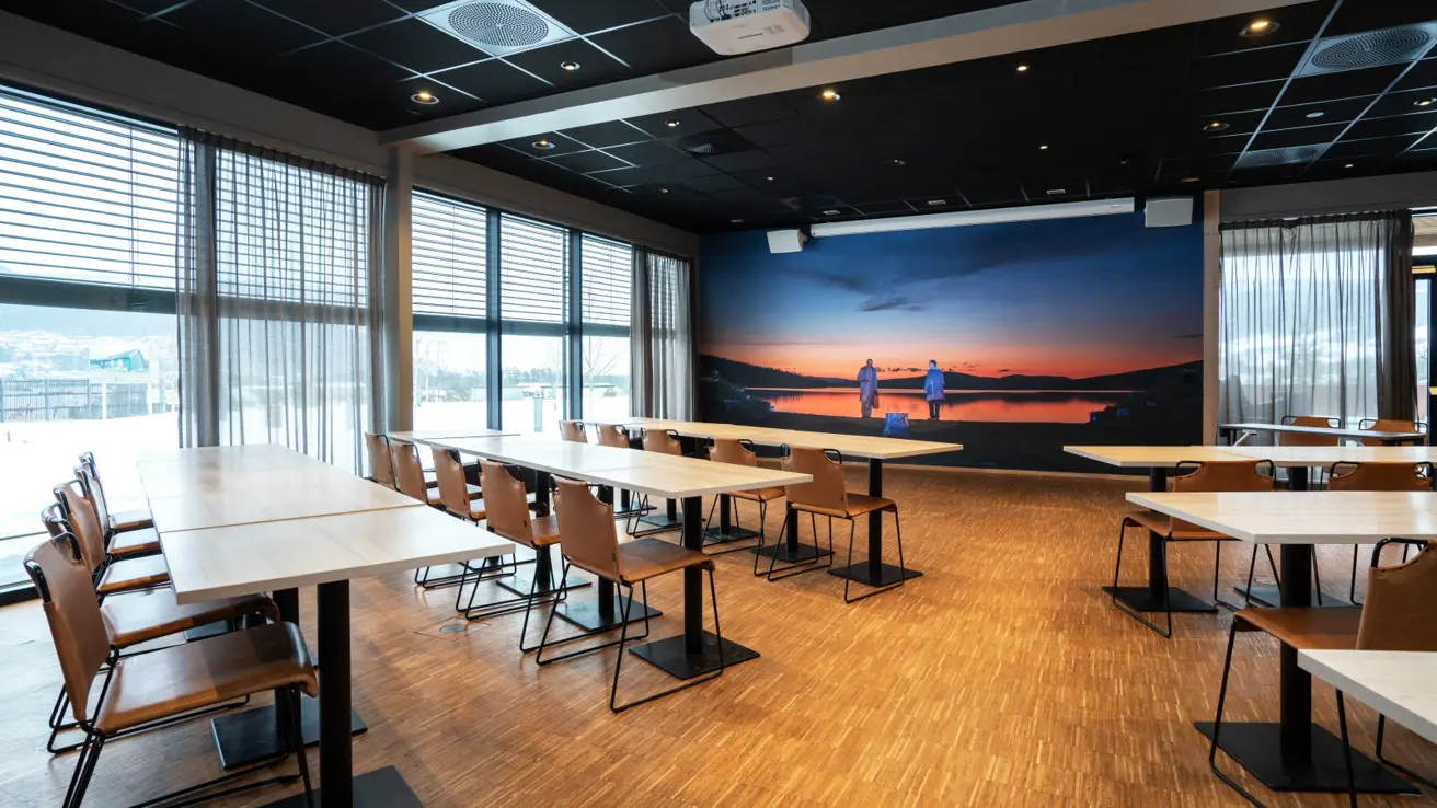 Mor Åse møterom i klasseromoppsett med midtgang mellom sitteplassene. Vinduer langs hele siden + noen i front. Bilde fra Peer Gynt i front.  Lerret i front.